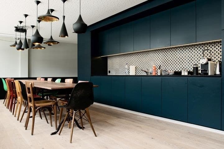 Café dining hall with navy-blue cabinetry, patterned brass backsplash, Tom Dixon black pendants and mismatched designer chairs